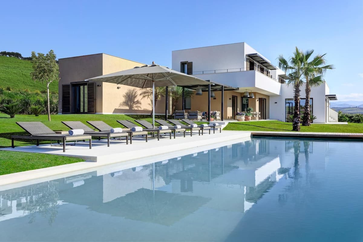 Una casa moderna con piscina, sillas de descanso y un patio cubierto.