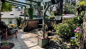 Un patio couvert aménagé avec des sièges, une pergola et un jardin où l’on trouve différentes plantes et fleurs.