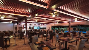 Un restaurant spacieux avec de hauts plafonds, des poutres apparentes et une piscine en arrière-plan.