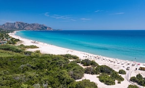 A coastal beach with a sandy shore, a clear blue sea, and a mountainous backdrop. - Nicolaus Prime Villas Resort (Ballao)