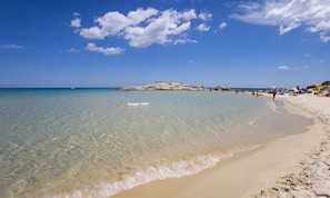 A beach with clear water, a sandy shore, and a rocky outcrop in the distance. - Nicolaus Prime Villas Resort (Ballao)