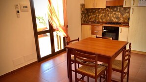 A compact kitchen with wooden cabinets, a tiled backsplash, and a dining area with a wooden table and chairs. - La Luna Nel Pozzo (Sciacca)