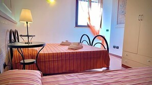 A hotel room with a bed, a small table with a lamp, a chair, and a window with curtains. - La Luna Nel Pozzo (Sciacca)