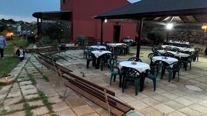 An outdoor patio area with tables and chairs, a wooden bench, and a building in the background. - La Luna Nel Pozzo (Sciacca)