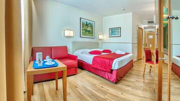 A hotel room with a bed, a red sofa, a small table with a tray, and a mirror.
