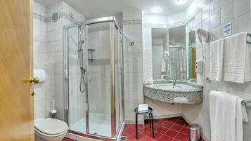 A bathroom with a glass-enclosed shower, a toilet, a sink with a mirror, and a red-tiled floor.