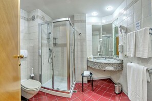 A bathroom with a glass-enclosed shower, a toilet, a sink with a mirror, and a red-tiled floor. - B&B Hotel Quarto D'altino (Quarto d'Altino)