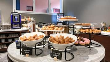 A bakery display with croissants and other pastries, a coffee machine, and a view of the outside.