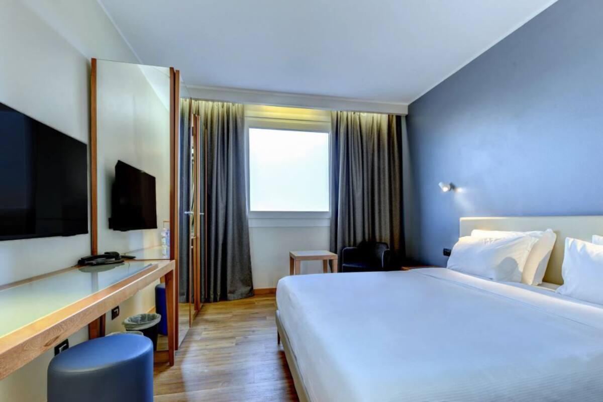 Een hotelkamer met een bed, een bureau met een flatscreen televisie, een stoel en een kleine tafel.