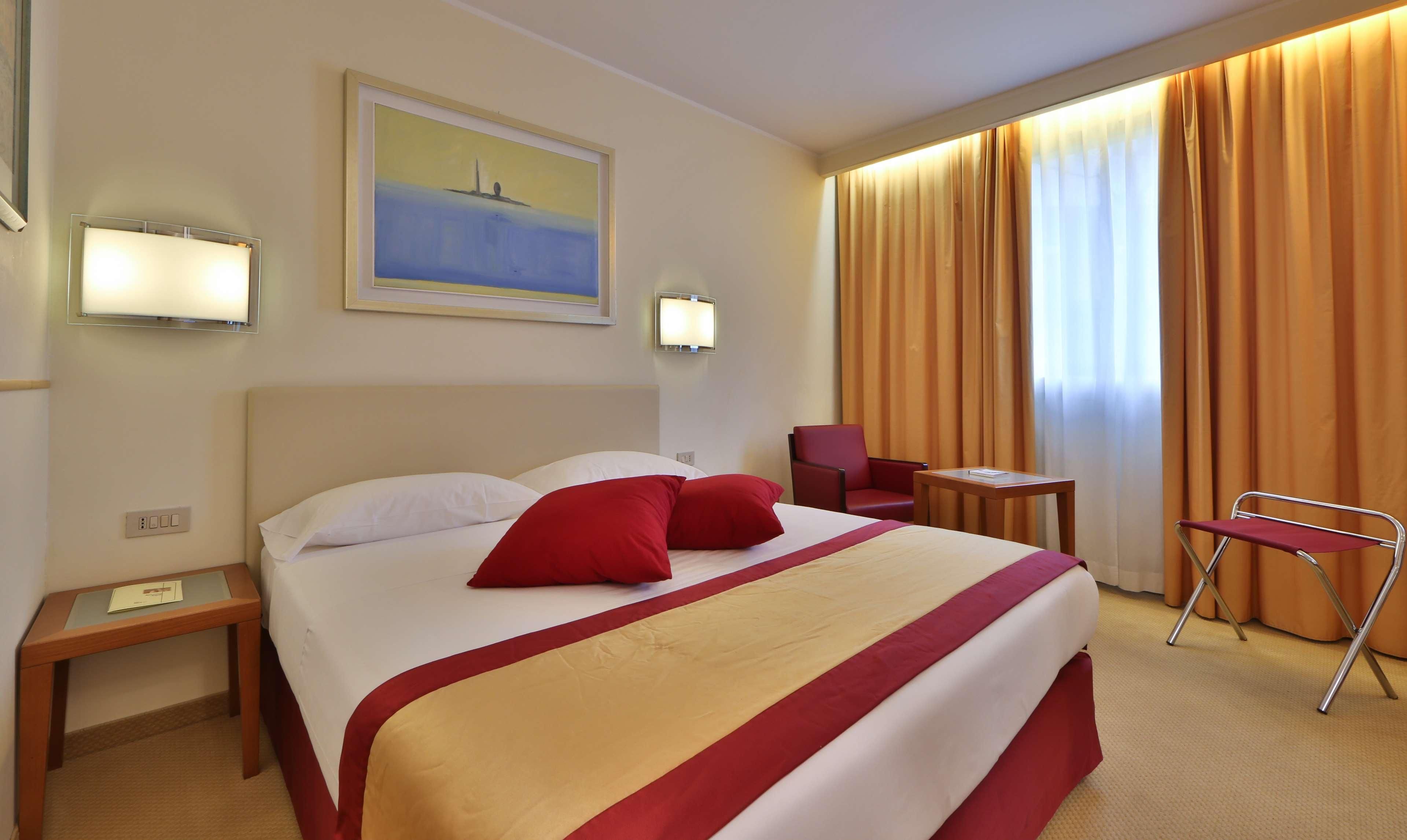 A hotel room with a large bed, two bedside tables, a desk, a chair, and a painting on the wall.