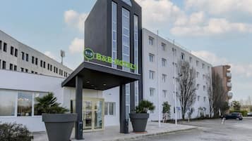 A B&B hotel with a modern facade, large potted plants, and a clear sky.