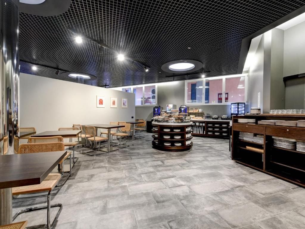 A modern cafe with a central round table, seating area with chairs, and a counter with display cases.