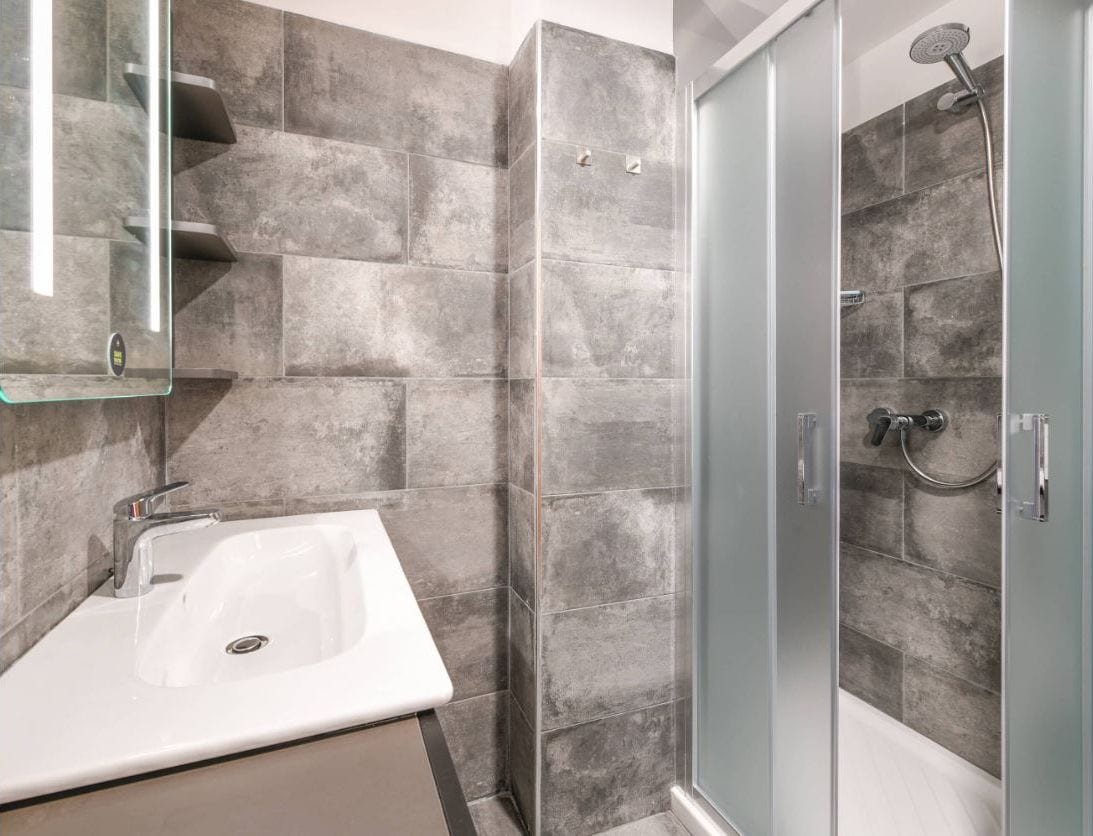 A bathroom with a white sink, a glass shower enclosure, and grey tiled walls.