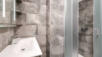 A bathroom with a white sink, a glass shower enclosure, and grey tiled walls.