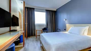 A hotel room with a bed, a desk, a chair, a TV, and a window with curtains.