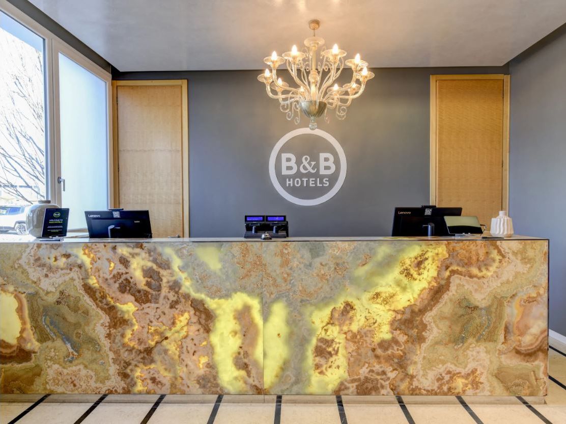 Un comptoir d’accueil avec un plateau en marbre, un lustre et une enseigne B&B Hotels.