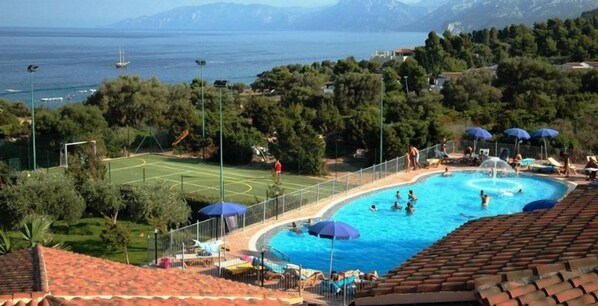 A swimming pool with a view of the sea and mountains, surrounded by trees and umbrellas. - Hotel La Conchiglia (Dorgali)