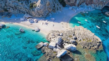 An aerial view of a coastal area with clear turquoise waters, rocky formations, and a sandy beach.