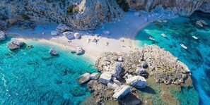 An aerial view of a coastal area with clear turquoise waters, rocky formations, and a sandy beach. - Hotel La Conchiglia (Dorgali)