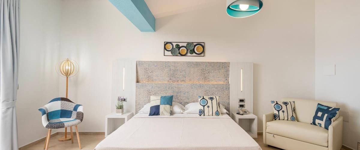A modern hotel room with a large bed, a sofa, a chair, and a decorative wall piece.