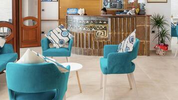 Een moderne hotel lobby met smaragdgroene banken en stoelen, een receptiebalie en een stenen open haard.