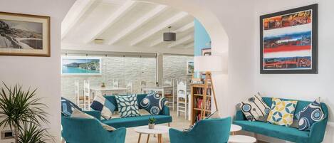 Una sala de estar moderna con sofás color turquesa, una mesa de centro y sillones. Se ve una estantería, una planta en maceta y un cuadro en la pared.
