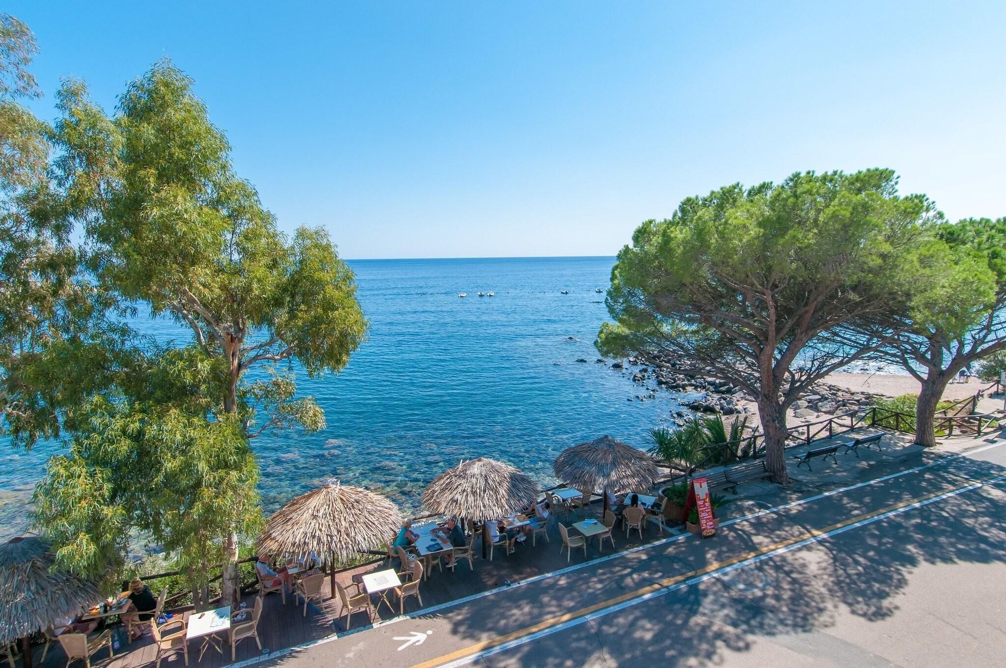 Un restaurante costero con terraza al aire libre y vistas al mar, con mesas y sombrillas.