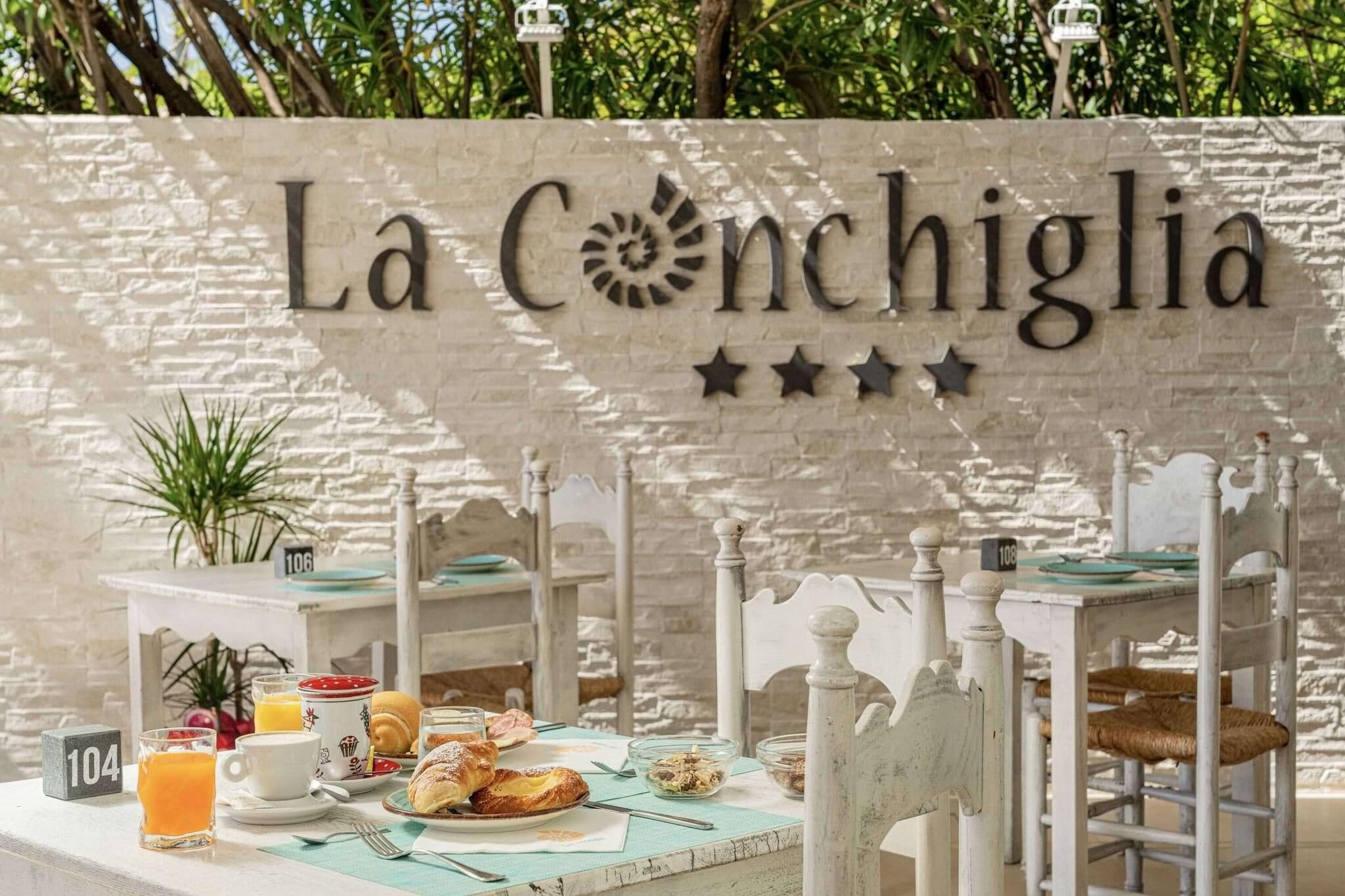 Ein Frühstücksbuffet mit einem Schild, auf dem 'La Conchiglia' steht, und nummerierten Tischen 104 und 108.