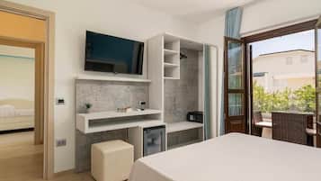 A modern hotel room with a large bed, a TV mounted on the wall, a small desk with a chair, a balcony with a wicker table, and a shower area.
