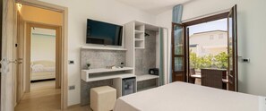 A modern hotel room with a large bed, a TV mounted on the wall, a small desk with a chair, a balcony with a wicker table, and a shower area. - Hotel La Conchiglia (Dorgali)