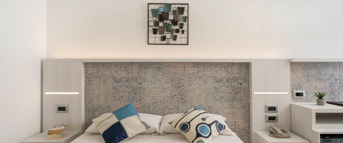 Une chambre à coucher moderne avec un grand lit, une tête de lit dotée d’un panneau arrière texturé, des tables de chevet avec des lampes et une œuvre d’art encadrée au-dessus du lit.