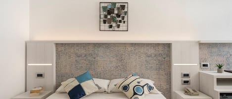 A modern bedroom with a large bed, a headboard with a textured back panel, bedside tables with lamps, and a framed artwork above the bed.