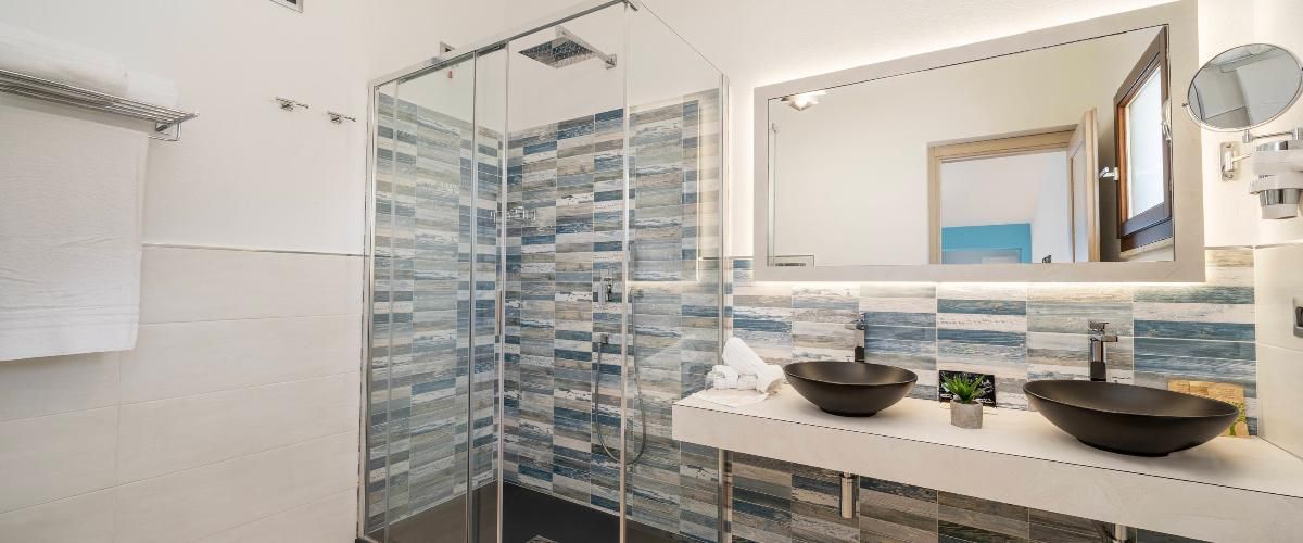 A modern bathroom with a glass shower enclosure, two vessel sinks, and a large mirror.