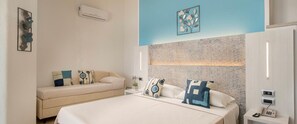A modern bedroom with a large bed, a sofa, and a small table with a phone. - Hotel La Conchiglia (Dorgali)
