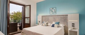 A hotel room with a bed, a nightstand, a wall-mounted lamp, a window with a view of the outdoors, and a door leading to a balcony. - Hotel La Conchiglia (Dorgali)