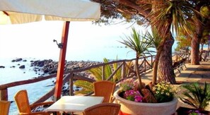 A seaside patio with wicker chairs and a table, overlooking the ocean and rocky shoreline. - Hotel La Conchiglia (Dorgali)