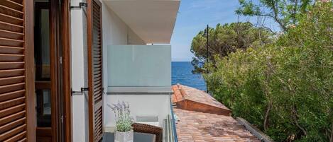 Un edificio moderno con puerta de cristal, un pequeño balcón con planta en maceta y vista al mar.