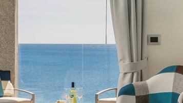 Una habitación con vista al mar, dos sillas, una mesa con una botella y una copa, y una cortina.