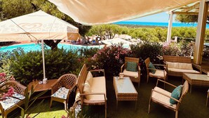 An outdoor patio area with wicker furniture, a stone wall, and a view of a pool and ocean.