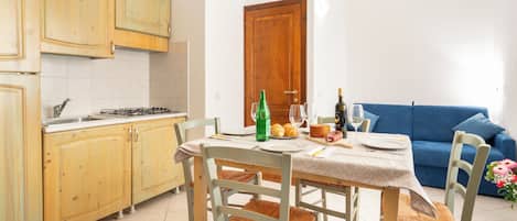 A compact kitchen with wooden cabinets, a dining table with chairs, and a blue sofa in the living area.