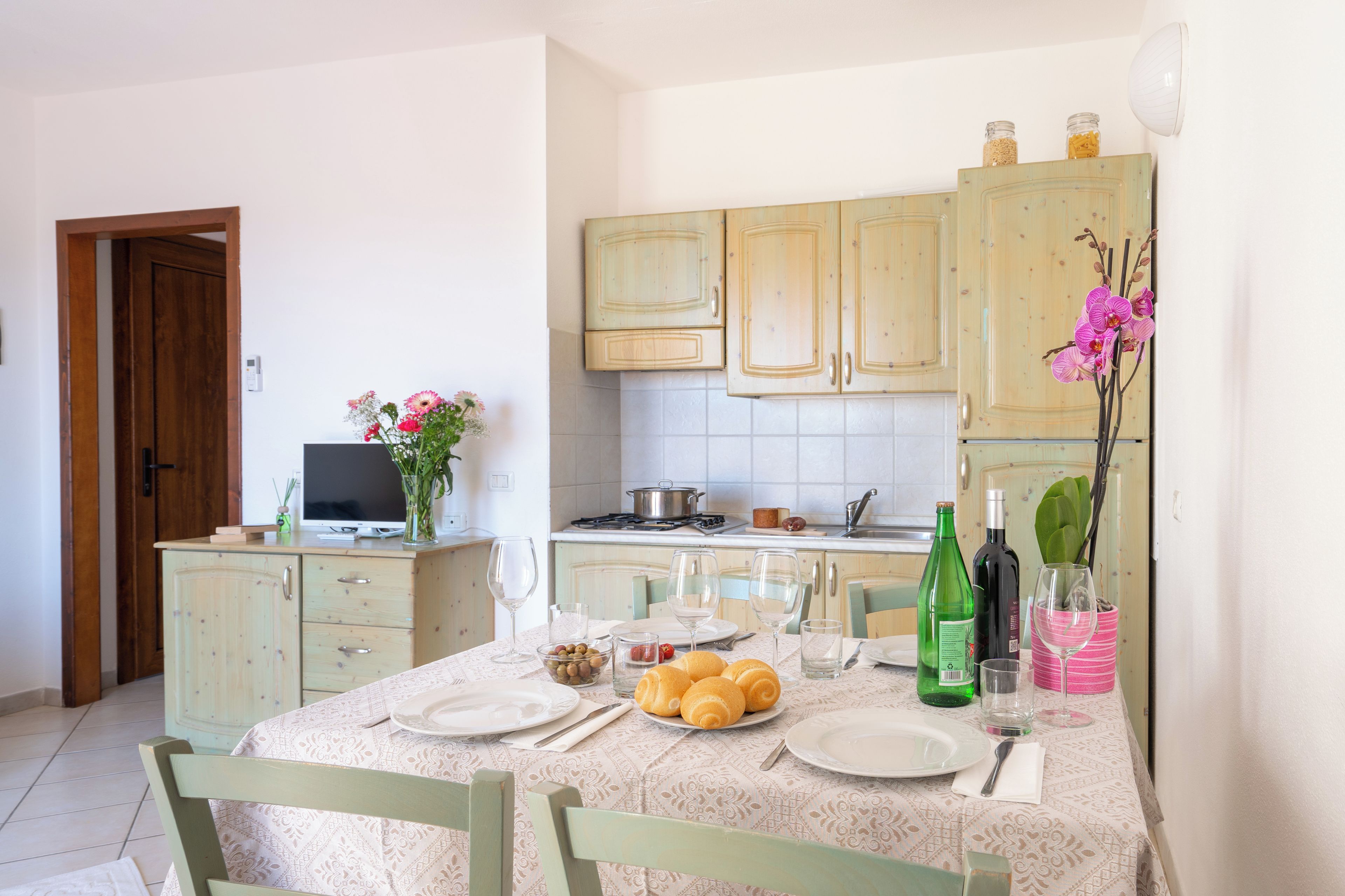 Un área de comedor con una mesa preparada para dos personas, un televisor y armarios de cocina al fondo.