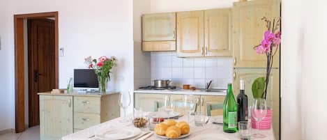 Un área de comedor con una mesa preparada para dos personas, un televisor y armarios de cocina al fondo.
