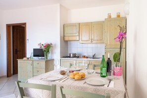 A dining area with a table set for two, a television, and kitchen cabinets in the background. - Le Corti del Turchese Residence (Badesi)