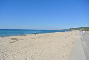 Une vaste plage de sable fin, sous un ciel bleu dégagé et une mer calme.