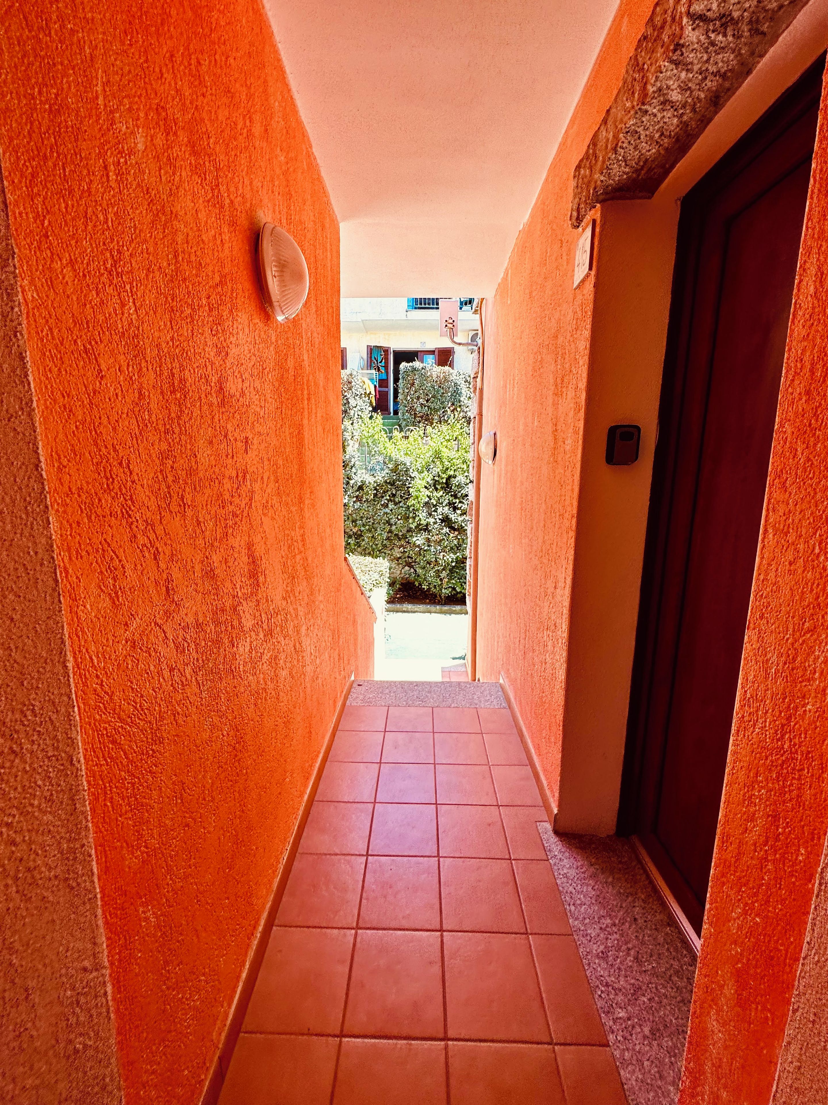 Un couloir aux murs orange et au sol carrelé, qui mène à une porte.
