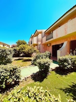 A building with multiple balconies, a green lawn, and surrounding greenery.