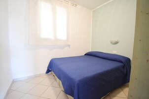 Ein kleines Zimmer mit einem Einzelbett, einer schlichten weißen Wand und einer Wand in Hellblau.