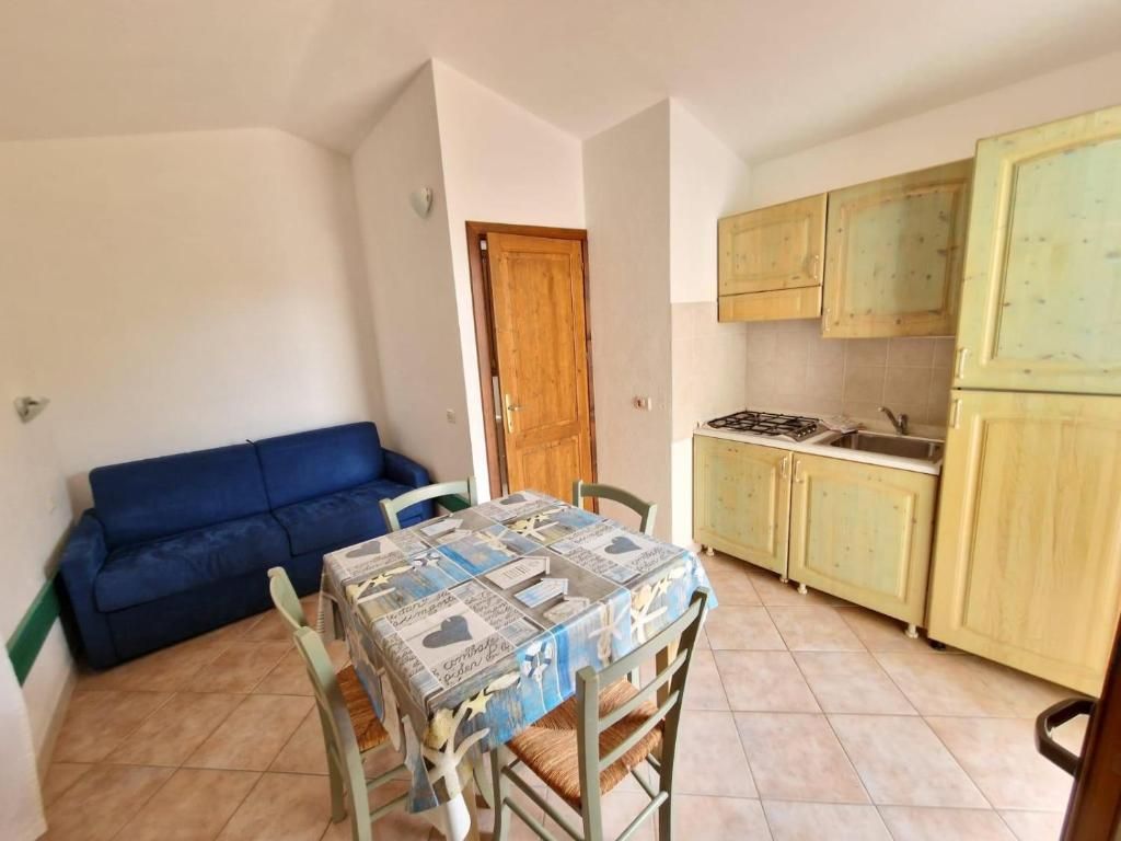 Un espace de vie compact comprenant une table à manger, des chaises, un canapé bleu et un coin cuisine avec des placards et une cuisinière.