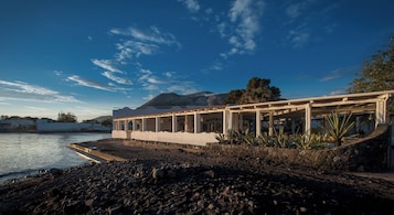 Un edificio costero con base de piedra, techo plano y una serie de columnas que sostienen un balcón.