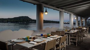 An outdoor dining area with tables set for two, overlooking a body of water and a distant hill. - Mari Del Sud Resort, Vulcano (Lipari)